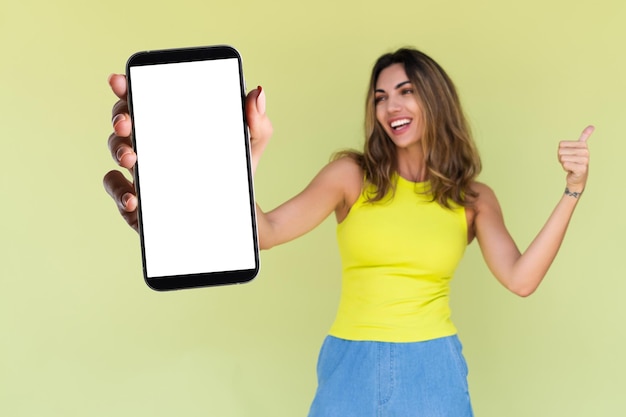 Foto jovem de roupa casual isolada em fundo verde segura um telefone com uma tela branca em branco