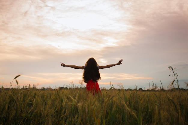 Jovem de saia vermelha está de pé com os braços estendidos em um campo Uma linda garota está de pé de costas para a câmera