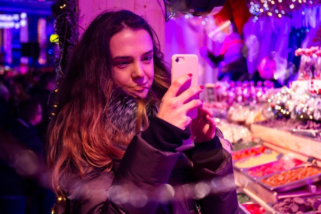 Jovem de trinta anos tirando uma foto de selfie na Feira de Natal sob luz neon roxa Foto noturna maravilhas de inverno conceito de feriados