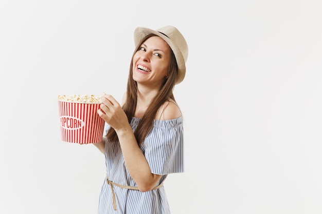 Jovem de vestido azul, chapéu, assistindo filme filme segurando, comendo pipoca de balde, isolado no fundo branco. Pessoas, emoções sinceras no cinema, conceito de estilo de vida. Área de publicidade. Copie o espaço.