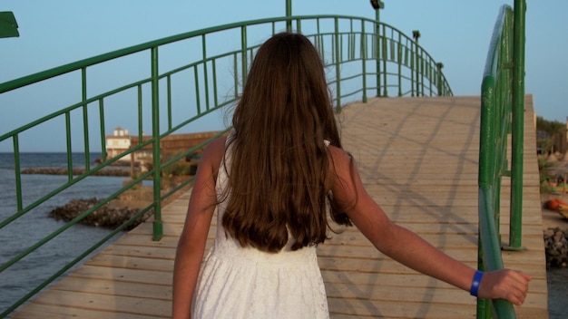 Jovem de vestido branco atravessando a ponte na hora do nascer do sol