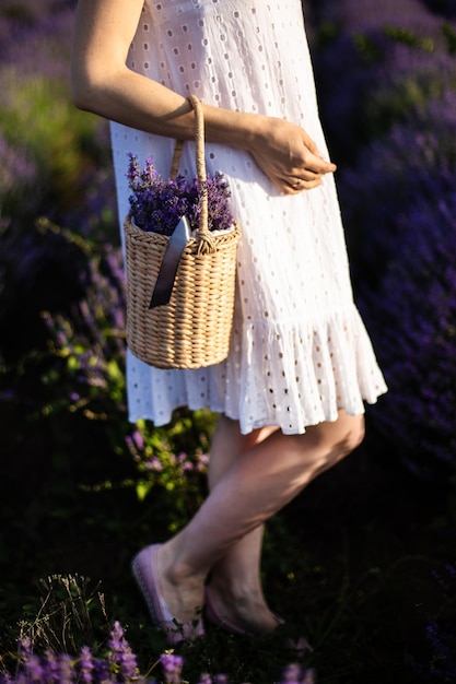 Jovem de vestido branco segurando uma cesta de palha com flores de lavanda