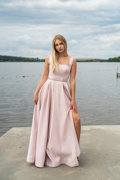 Jovem de vestido de noite rosa longo sozinha perto do lago no parque da cidade