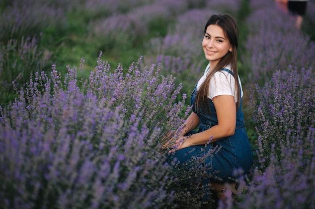 Jovem de vestido jeans sentado no campo de lavanda no verão Sorriso de menina bonita