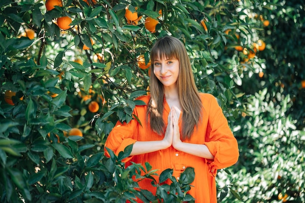 Jovem de vestido laranja está posando para a câmera segurando as mãos juntas no jardim laranja