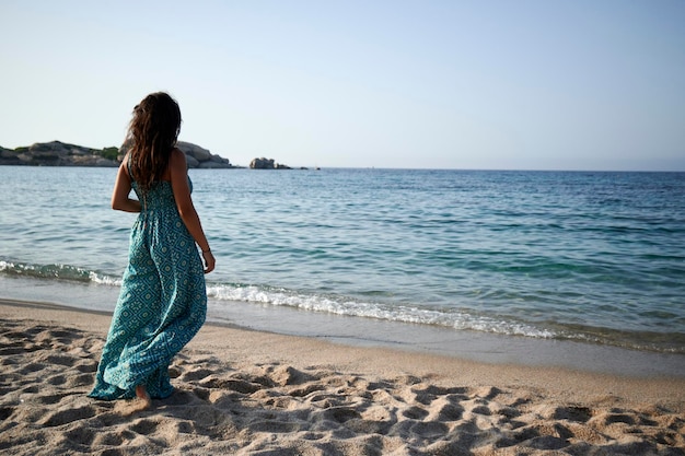 Jovem de vestido na praia tranquila admirando o horizonte sobre a água