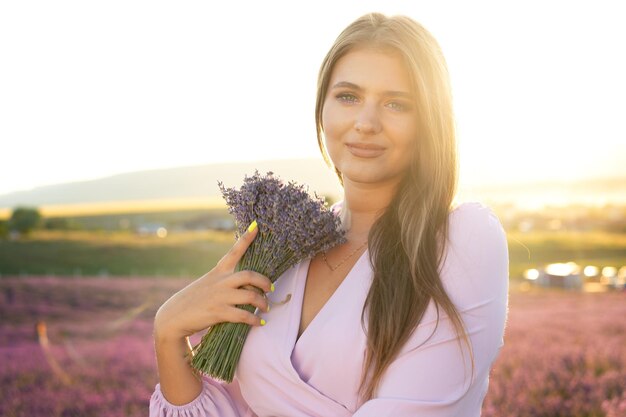 Jovem de vestido segurando o buquê de flores em pé no campo de lavanda