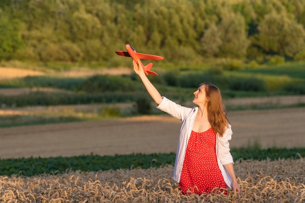 Jovem de vestido vermelho e camisa branca com modelo de um avião na mão campo de trigo Voos baratos