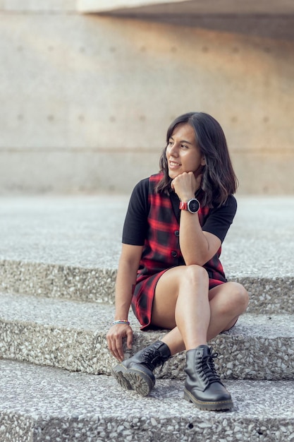 Jovem de vestido vermelho sentado nas escadas de um prédio olhando o horizonte com espaço de cópia