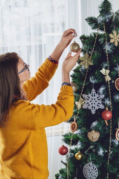 Jovem decorando árvore de natal segurando bola dourada