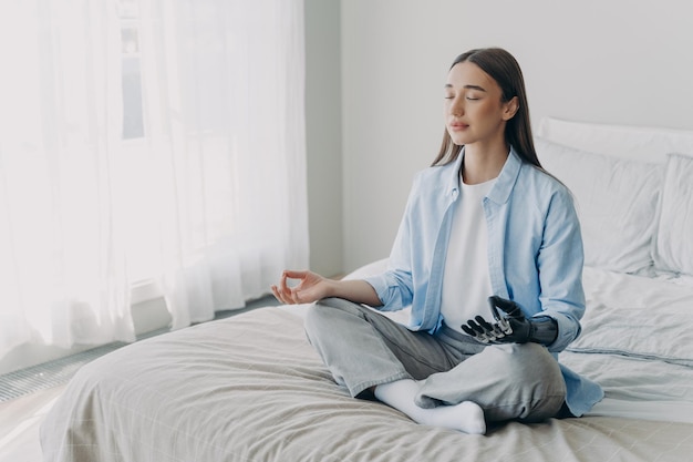 Jovem deficiente está praticando ioga em pose de lótus na cama em seu quarto Alívio de estresse em casa