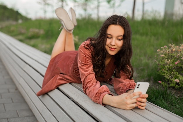 jovem deitada em um banco com um telefone celular