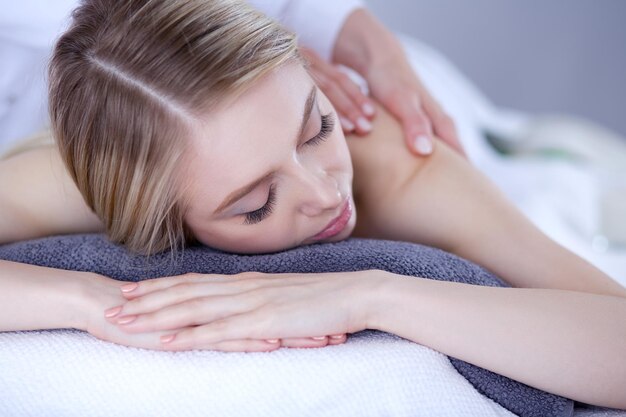 Jovem deitada em uma mesa de massagem relaxando com os olhos fechados salão de spa mulher