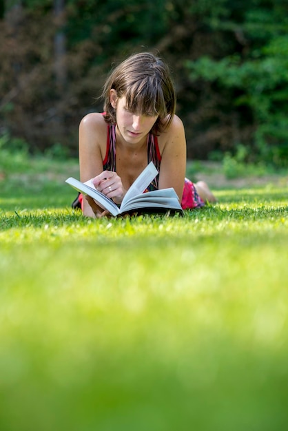 Jovem deitada na grama verde lendo um livro