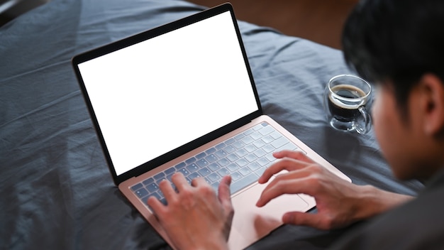 Jovem deitado na cama e navegando na internet com o computador laptop pela manhã.