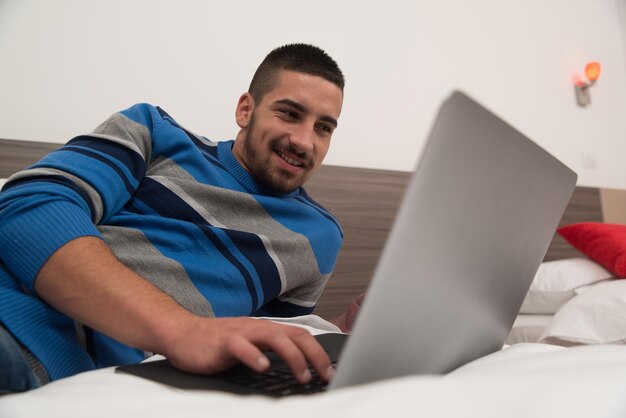 Jovem deitado na cama e se divertindo com o laptop no quarto