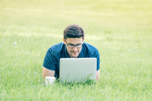 Jovem deitado na grama e usando o laptop