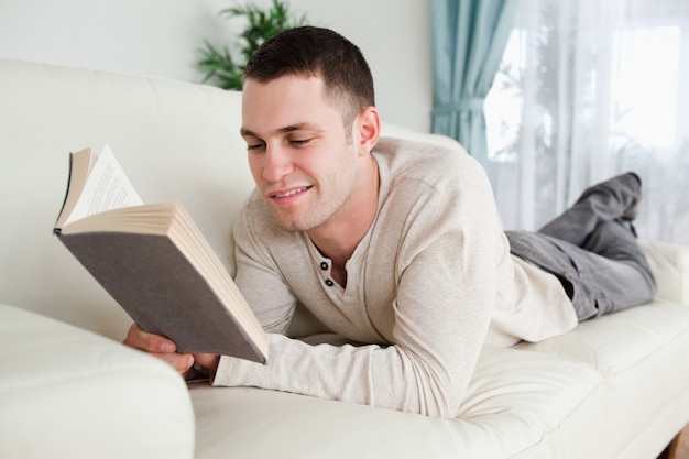 Jovem, deitado no sofá, para ler um livro