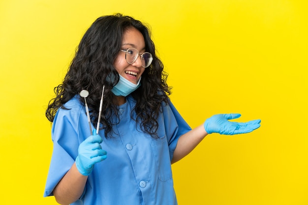 Jovem dentista asiático segurando ferramentas sobre um fundo isolado com expressão de surpresa enquanto olha para o lado