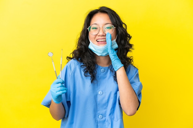 Jovem dentista asiático segurando ferramentas sobre um fundo isolado, gritando com a boca aberta