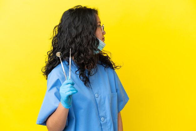 Jovem dentista asiático segurando ferramentas sobre um fundo isolado, olhando para o lado