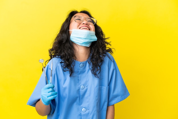 Jovem dentista asiático segurando ferramentas sobre um fundo isolado rindo