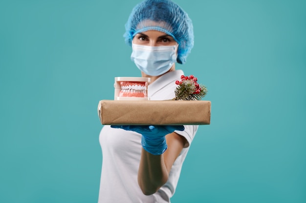 Jovem dentista com um chapéu e uma máscara tem um presente de natal na palma da mão.