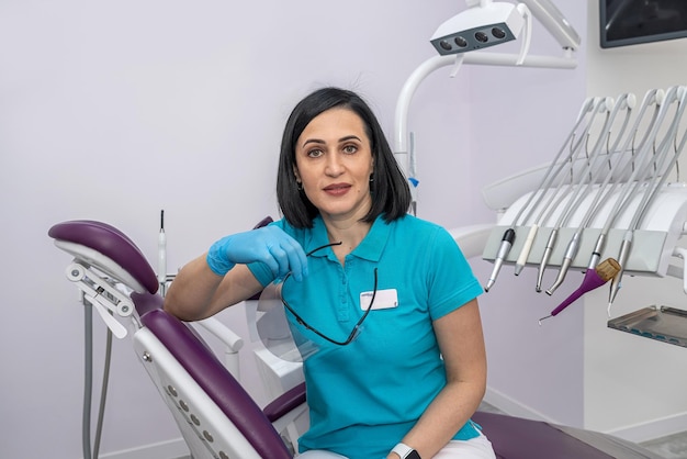 Jovem dentista feminina em uma clínica privada com equipamento odontológico moderno em pé e sorrindo