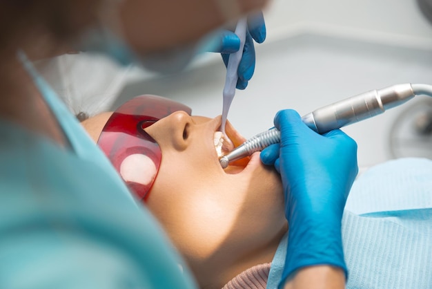 Jovem dentista feminina usando máscara e luvas descartáveis está no processo de trabalho com um paciente com a boca aberta