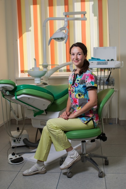 jovem dentista na cadeira odontológica ao lado do painel odontológico