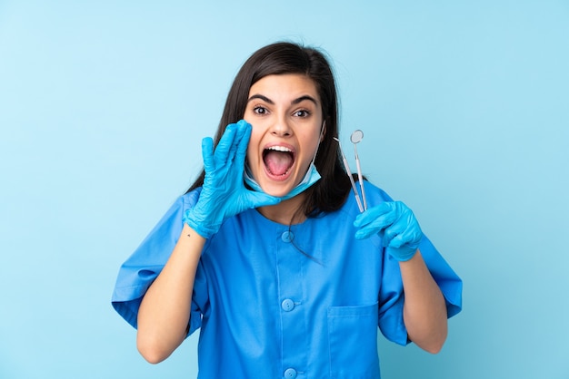 Jovem dentista segurando ferramentas e gritando azul isolado com a boca bem aberta