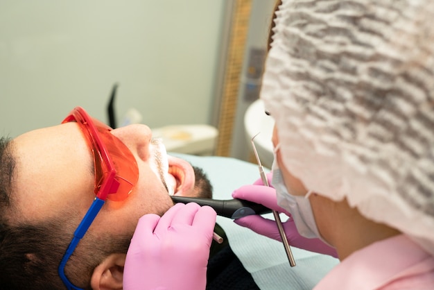 Foto jovem dentista trata paciente um homem.
