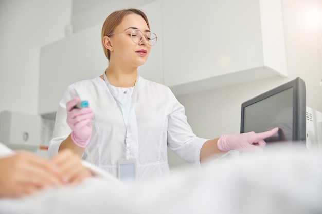 Jovem dermatologista caucasiana com jaleco e luvas esterilizadas usando cosmetologia de hardware