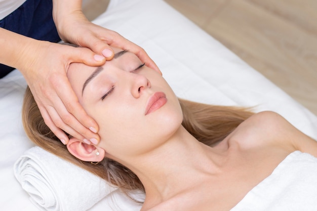 Jovem, desfrutando de massagem no salão spa. Massagem de rosto. Closeup de jovem recebendo tratamento de massagem spa no salão de beleza spa. Cuidados com a pele e o corpo. Tratamento de beleza facial.