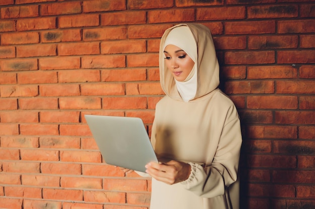 Jovem designer asiática muçulmana usando tablet gráfico enquanto trabalha com computador no estúdio ou escritório