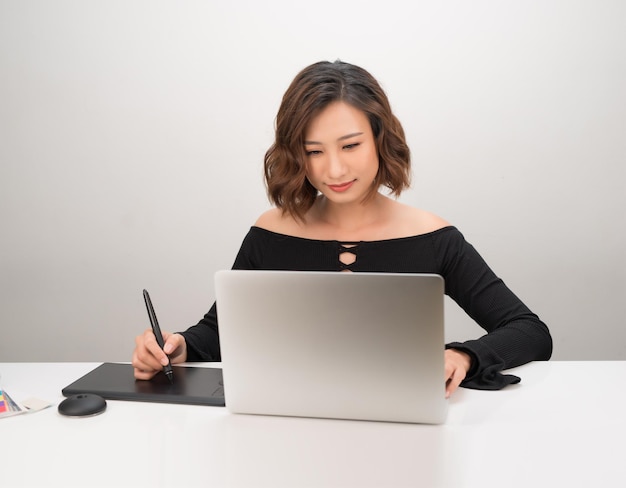 Jovem designer asiática usando tablet gráfico enquanto trabalhava com computador