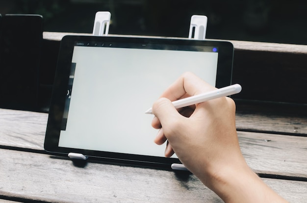 Jovem designer criativo segurando caneta stylus desenhando na tela do tablet digital enquanto está sentado no parque