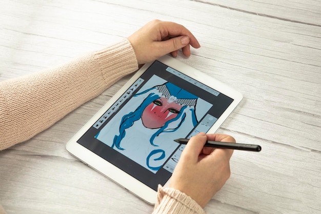 Jovem designer criativo segurando uma caneta stylus desenhando na tela do tablet digital na mesa de madeira com c