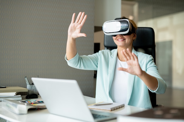 Jovem designer de sucesso assistindo uma apresentação virtual e tocando a tela enquanto está sentado à mesa no escritório