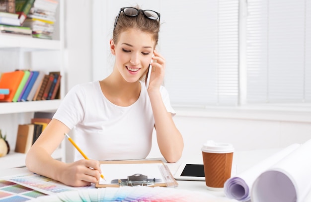 Jovem designer feminina falando por telefone e fazendo lista de verificação