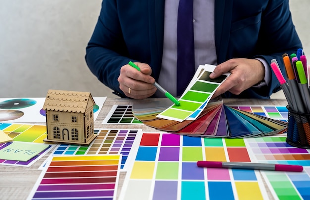 Jovem designer gráfico ou interior de terno, escolhendo a cor de amostra de amostra ou guia de paleta de catálogo no local de trabalho. designer gráfico com amostras de paleta de cores de tinta na mesa, close-up