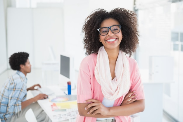 Jovem designer sorrindo para a câmera com um colega atrás dela