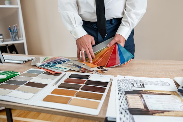 jovem designer trabalha com planos e esboços de casa e paleta de cores no escritório