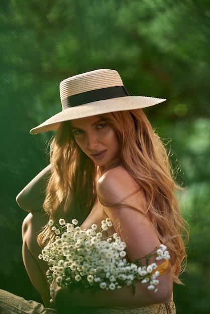 Foto jovem deslumbrante em uma roupa de verão e com flores brancas nas mãos na floresta