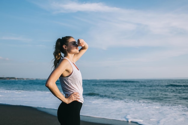 Jovem desportista com a mão na cintura cobrindo o rosto do sol na praia do mar