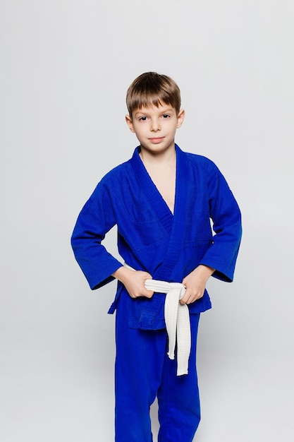 Jovem desportista de quimono azul para sambo judô posando em fundo branco olhando direto