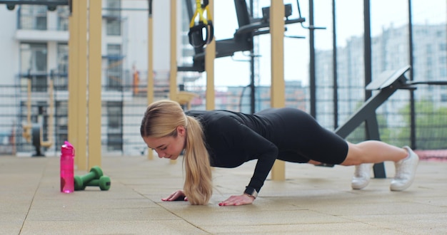 Jovem desportista fazendo flexões como parte do treinamento de treino Mulher em roupas esportivas treinando ao ar livre fazendo treino de força