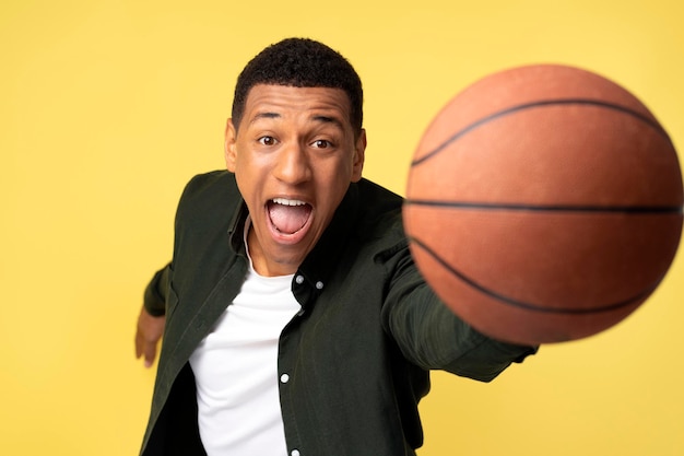 Jovem desportista jogando bola de basquete para a câmera sobre fundo amarelo isolado