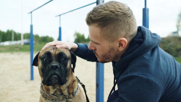 Jovem desportivo abraça e joga seu cachorro bullmastiff ao ar livre na natureza