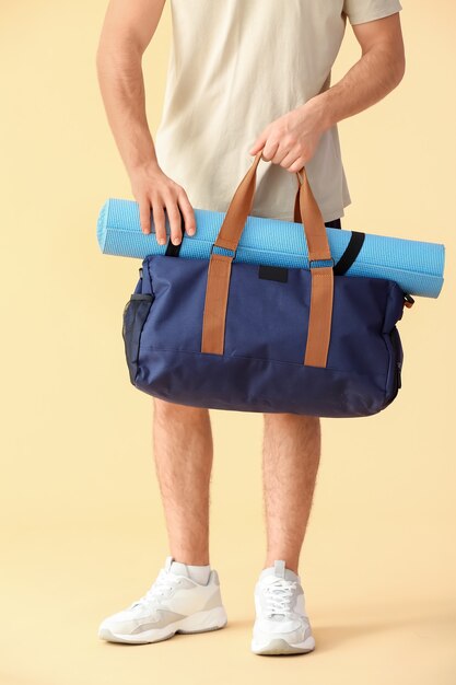 Jovem desportivo com bolsa e tapete de ioga bege